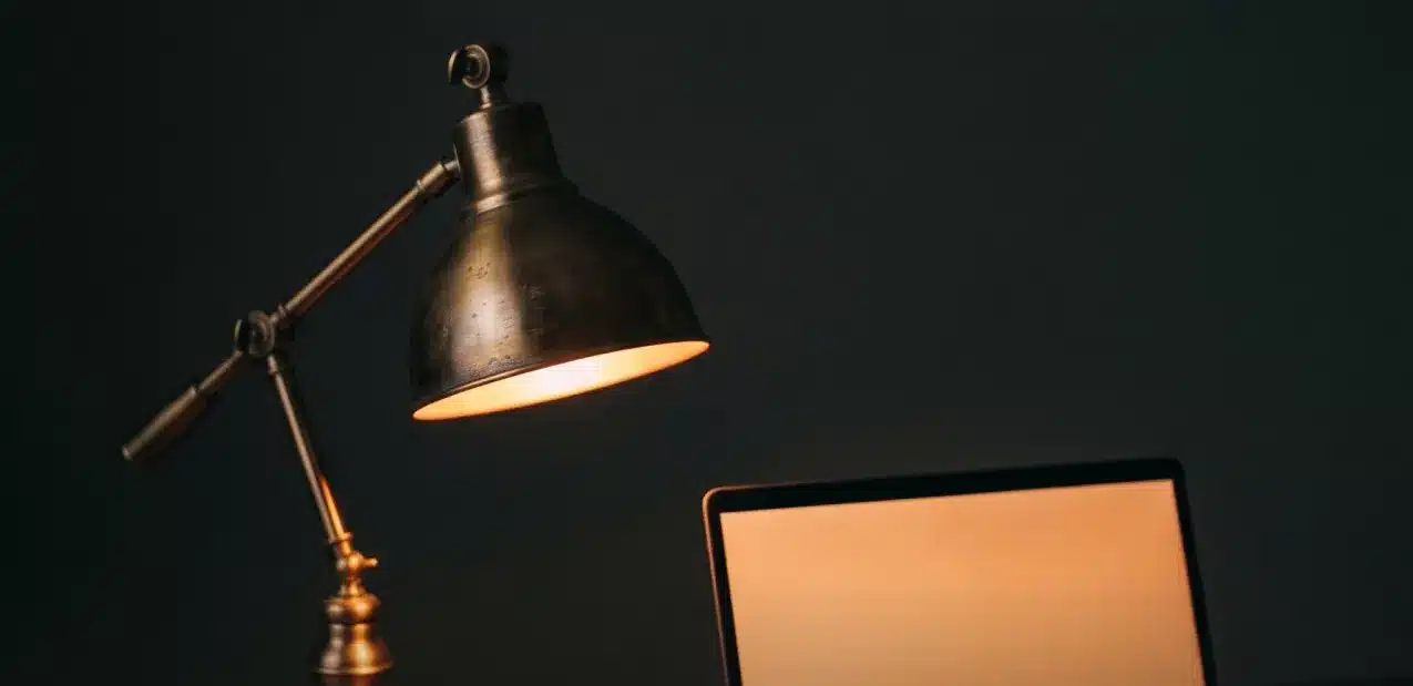 Brass desk lamp lighting an open laptop in a dark studio
