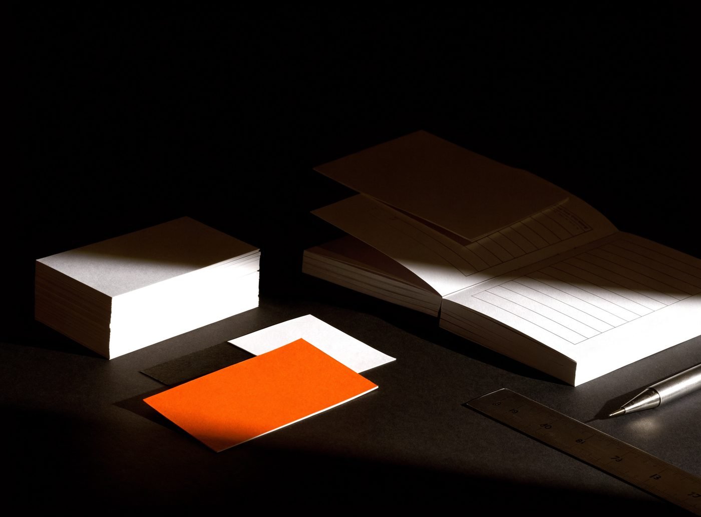 Blank business cards, paper colour chips and an unmarked guide booklet on a dark studio surface under hard raking light
