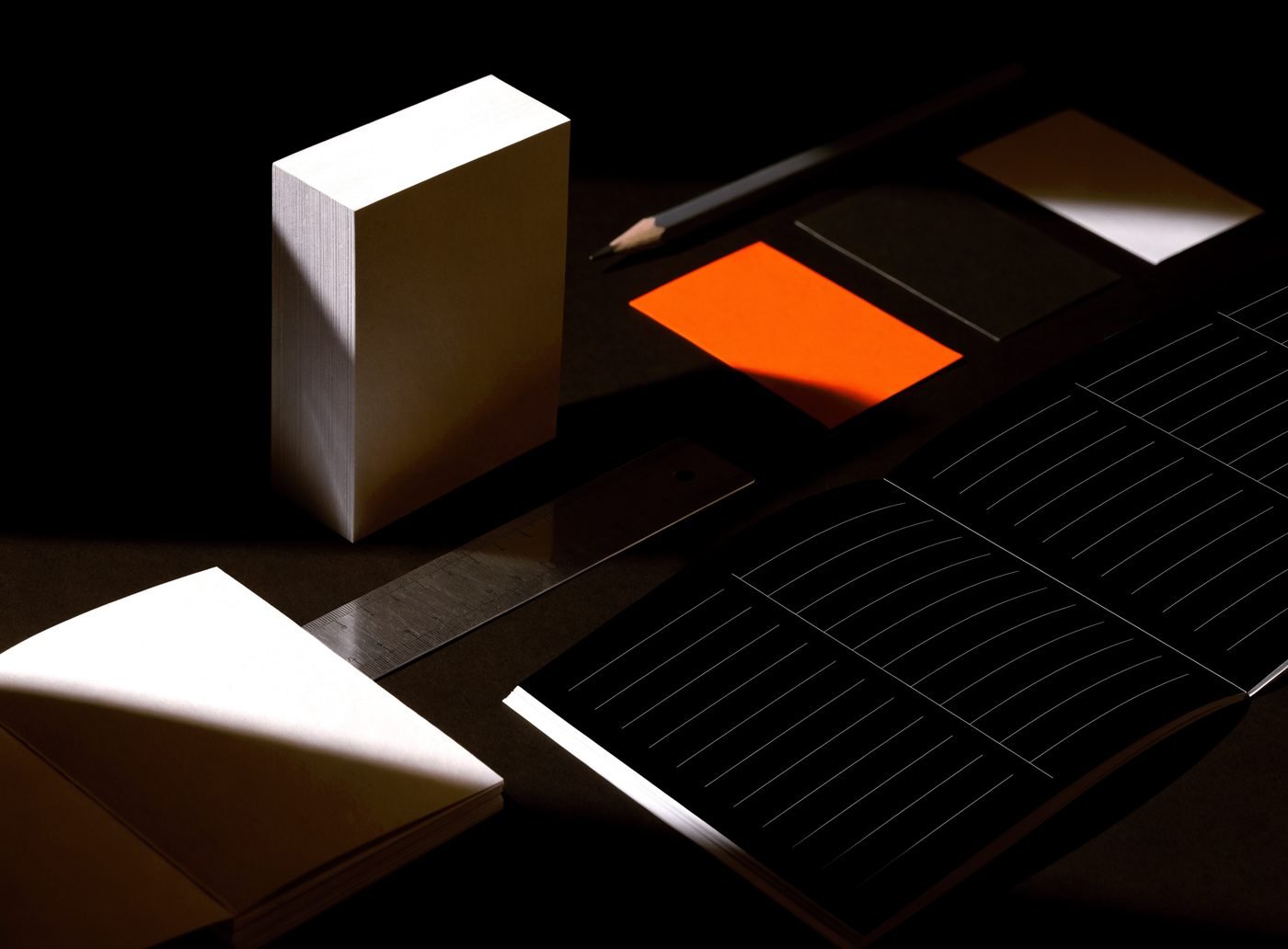 Stacked blocks of blank card stock of different heights beside an orange card and an open blank grid book, on a dark surface
